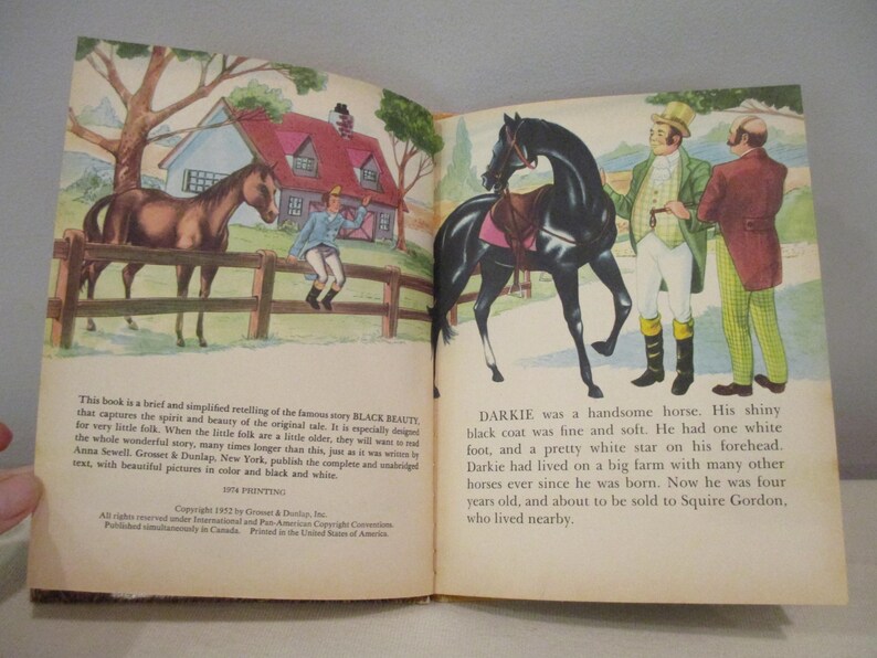 May include: Vintage children's book illustration featuring two horses, one brown and one black, with a boy and two men. The book is open, displaying colorful images and text about the story of Black Beauty.