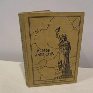 May include: A vintage book titled "Modern Americans" with a brown cover and a black and white illustration of the Statue of Liberty. The book is published by the Laurel Book Company.