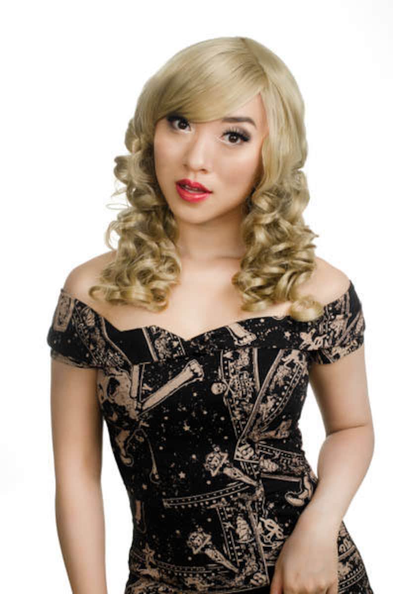 Pode incluir: Uma mulher com cabelo loiro encaracolado est&aacute; vestindo um vestido preto e dourado de ombro a ombro com uma estampa de cartas de tar&ocirc; e outros s&iacute;mbolos.