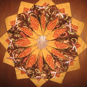 May include: A brown and orange fabric wreath with pink bows. The wreath is made of multiple fabric pieces sewn together in a circular shape.