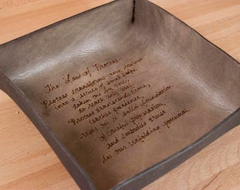 May include: A brown leather tray with a quote about the law of process inscribed on the inside. The quote reads: "The Law of Process. Process transforms any journey into a series of small steps, taken one by one, to reach any goal. Process transcends time, teaches patience, rests on a solid foundation, of careful preparation, and embodies trust in our unfolding potential."
