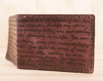 May include: A brown leather wallet with a handwritten message on the front. The message reads: "naabersting through my skin, peactancy in bory Core word dearing the bringing au to disser You are right, every sras mesmerizingly You hold de arney of vass The righe day, adding up to ac I go one my Grass You are smag."