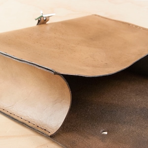 May include: A brown leather bag with a flap closure and a silver clasp. The bag is open and the inside is visible.