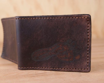 May include: A brown leather wallet with a stitched edge and a footprint design embossed on the front.