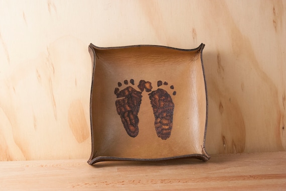 Baby footprints pressed into antique leather — a completely unexpected twist on the valet tray that turns it into a dad keepsake unlike anything else in this category.