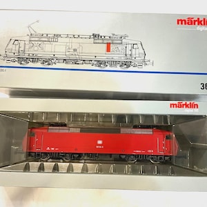 May include: A Märklin digital HO model train locomotive in a red finish, housed in a silver box with a clear plastic window. The packaging features the Märklin logo, the number 3654, and a line drawing of a BR 120.1 electric locomotive.