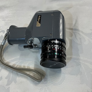 May include: A gray vintage Saligor 201 Super 8 film camera with a black lens and a gray strap.