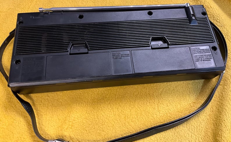 Puede incluir: Radio port&aacute;til negro y plateado con una correa negra. La radio tiene una antena negra y plateada y una rejilla de altavoz negra. La radio tiene una carcasa de pl&aacute;stico negro con un ribete plateado. La radio tiene una correa negra con una hebilla plateada. La radio tiene un panel de control negro y plateado con una perilla plateada. La radio tiene una pantalla negra y plateada con una luz de fondo plateada. La radio tiene un interruptor de encendido negro y plateado. La radio tiene un control de volumen negro y plateado. La radio tiene una perilla de sintonizaci&oacute;n negra y plateada. La radio tiene una toma de auriculares negra y plateada. La radio tiene una toma de entrada auxiliar negra y plateada. La radio tiene un compartimento para bater&iacute;as negro y plateado. La radio tiene una antena negra y plateada.