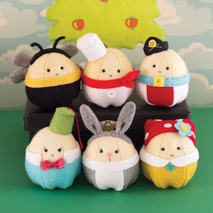 May include: Six felt stuffed toys shaped like onions, each wearing a different costume. The costumes include a bee, a chef, a pirate, a bunny, a gentleman, and a mushroom.