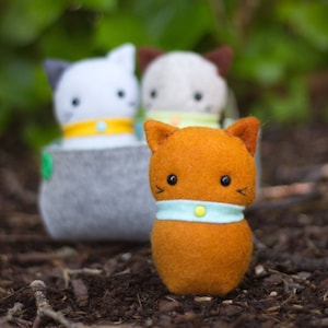May include: Three felt cat toys. One white cat with yellow collar, one gray cat with green collar, and one orange cat with blue collar.