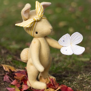 May include: A yellow felt bunny toy with a yellow and white striped headband and a white felt butterfly in its hand.