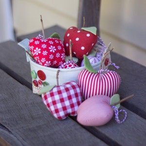 May include: A white ceramic container with red and white polka dot fabric apples, red and white gingham fabric apples, and a pink fabric apple. The container has a red and white polka dot fabric handle.