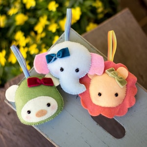 May include: Three felt animal ornaments, a green monkey, a blue elephant, and an orange lion. Each ornament has a bow and is ready to hang.