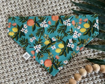 May include: A turquoise blue bandana with a lemon and flower print. The bandana features yellow lemons, white flowers, and green leaves on a turquoise blue background.