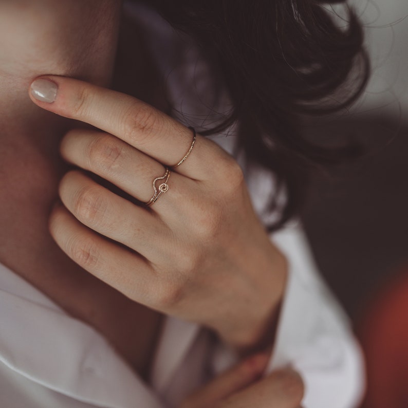 Puede incluir: Dos anillos de oro en un dedo. El anillo superior es una banda fina. El anillo inferior es una banda curva con un peque&ntilde;o c&iacute;rculo en el centro.