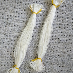 May include: Two white cords tied together with yellow rubber bands. The cords are lying on a gray textured surface.
