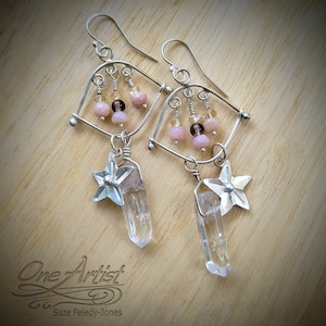 May include: Silver earrings with a geometric design, featuring pink and brown beads, clear quartz crystals, and star-shaped charms.