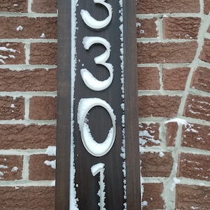 May include: A wooden sign with a dark brown frame and white numbers, reading "3301", covered in snow.