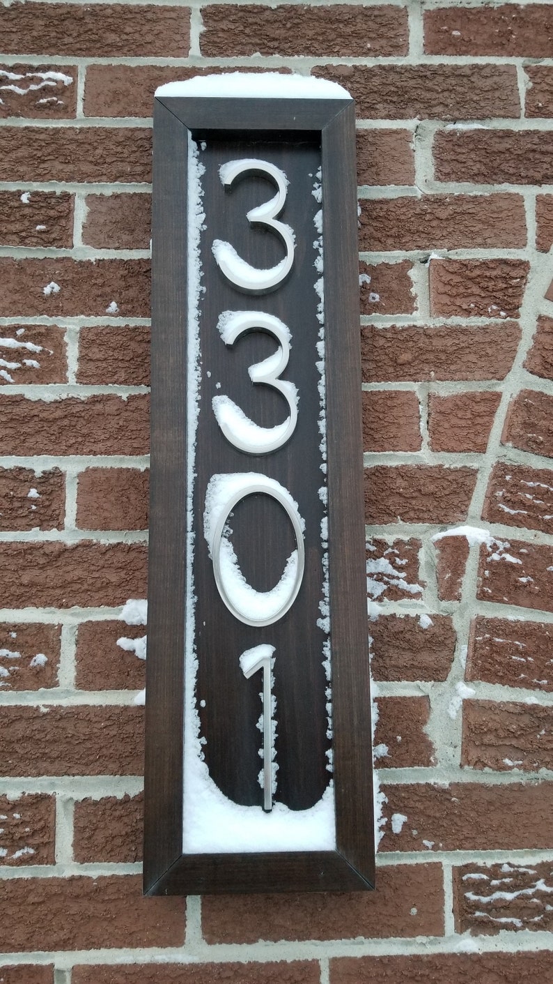 May include: A wooden sign with a dark brown frame and white numbers, reading "3301", covered in snow.