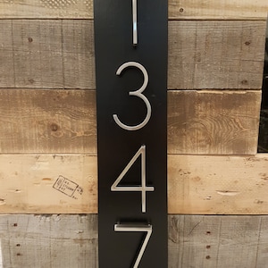 May include: A black wooden sign with silver metal numbers 1347. The sign is mounted on a wooden wall.