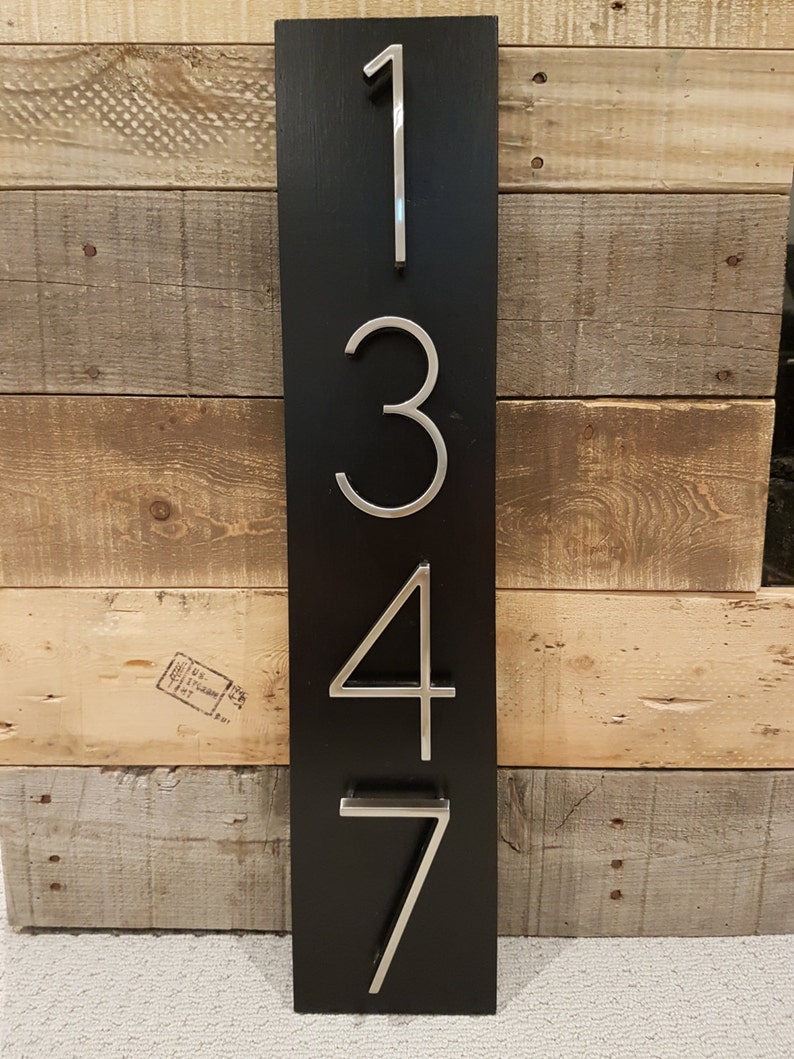 May include: A black wooden sign with silver metal numbers 1347. The sign is mounted on a wooden wall.