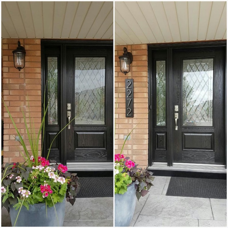 May include: A black front door with a glass panel and a black doormat. A potted plant with pink flowers is in front of the door. The house number 2272 is displayed on the brick wall next to the door.