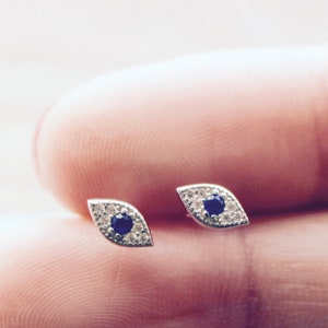 Puede incluir: Un par de pendientes de plata con una piedra preciosa azul y diamantes blancos en forma de ojo.