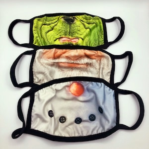 May include: Three reusable face masks with different character designs. The top mask features a green Grinch-like character, the middle mask features a white-bearded Santa Claus, and the bottom mask features a snowman.