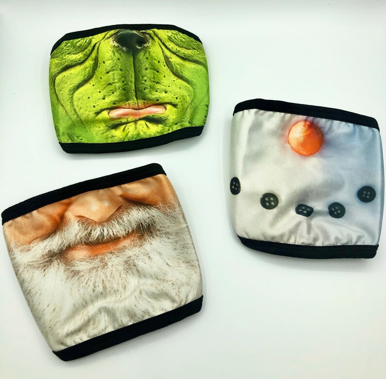 May include: Three reusable face masks with different designs. The first mask is green with a cartoon Grinch face. The second mask is white with a cartoon snowman face. The third mask is white with a cartoon Santa Claus face.