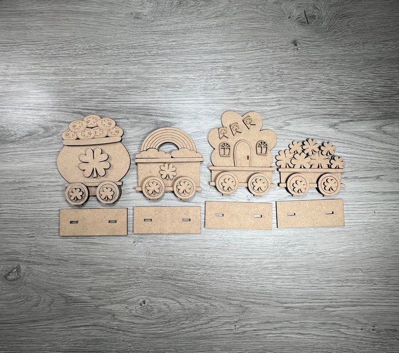 May include: Wooden train set with four cars, each decorated with a different Irish theme. The first car is a pot of gold, the second is a shamrock, the third is a leprechaun's house, and the fourth is a pile of shamrocks.