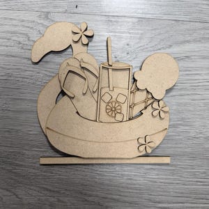 May include: A flat, laser-cut wooden cutout featuring a flamingo-shaped pool float, a pair of flip-flops, a tall glass with a straw and ice cubes, and an ice cream cone. The design includes small flower accents and a rectangular base stand.