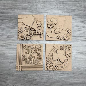 May include: Four square wooden St. Patrick's Day decorations. Each features a different design: a heart with the word "Lucky", a leprechaun boot, the phrase "Luck of the Irish", and a horseshoe with a shamrock and the word "wish".