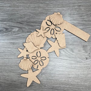 May include: A set of wooden cutouts in the shape of seashells and starfish. The cutouts are unfinished and ready to be painted or stained.