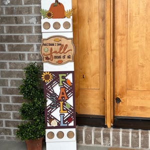 May include: A white wooden sign with a fall theme. The sign has a pumpkin, sunflowers, and the words "I think I love fall most of all". The sign also has a cutout of the word "FALL" with different colored letters and a sunflower design.