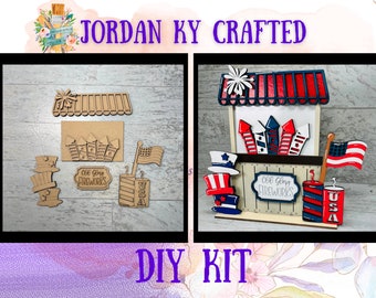 May include: A DIY craft kit featuring a wooden cutout of a fireworks stand with red, white, and blue accents. The kit includes various pieces to assemble the stand, including fireworks, stars, and a sign that reads "Old Glory Fireworks".