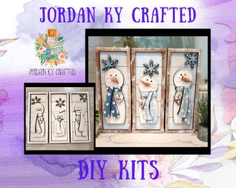 May include: Three rectangular wooden signs featuring snowman figures with orange carrot noses, blue scarves with white patterns, and snowflake accents. The snowmen are displayed in both finished painted versions and unpainted wood DIY kits.
