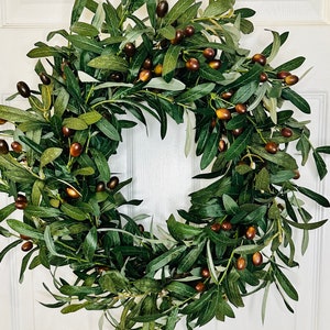 May include: A green olive branch wreath with brown olives. The wreath is made of artificial greenery and is perfect for decorating a door or wall.