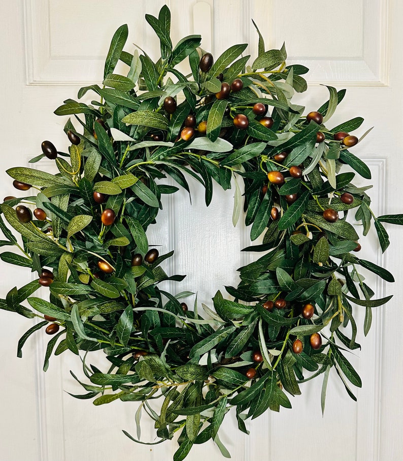 May include: A green olive branch wreath with brown olives. The wreath is made of artificial greenery and is perfect for adding a touch of nature to your home decor.