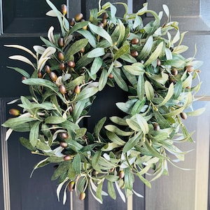 May include: A green olive branch wreath with brown olives. The wreath is made of artificial leaves and is perfect for decorating a door or wall.