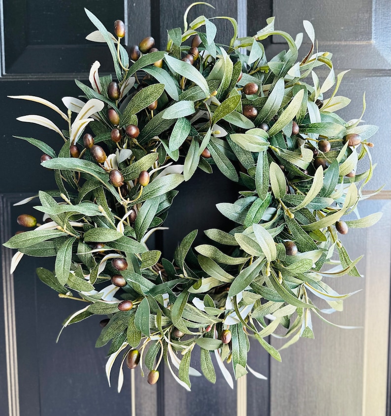 May include: A green olive branch wreath with brown olives. The wreath is made of artificial leaves and is perfect for decorating a door or wall.