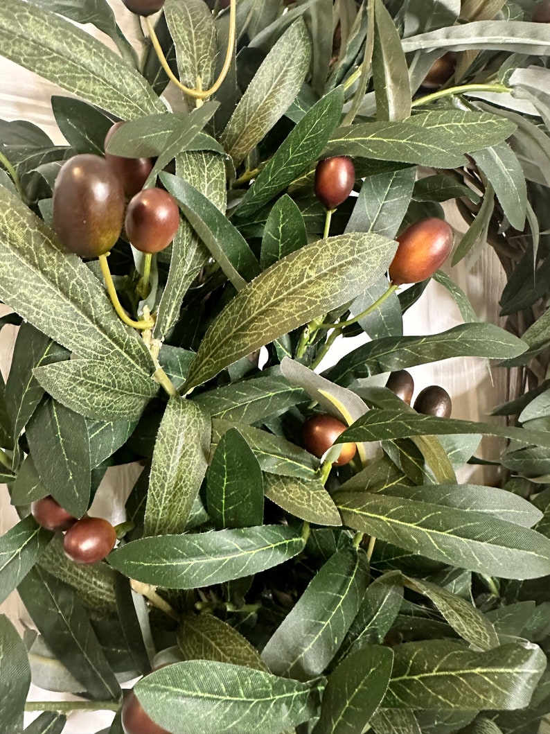 May include: A close-up of a green olive branch with brown olives. The branch is made of artificial materials and is perfect for adding a touch of nature to your home decor.