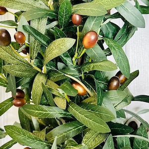 May include: A close-up of a green olive branch wreath with brown olives. The wreath is made of artificial leaves and olives.