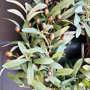 May include: A green olive branch wreath with dark brown olives. The wreath is made of artificial leaves and olives.