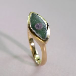 May include: A gold ring with a green and gray gemstone set in a marquise shape.