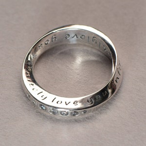 May include: A silver ring with a twisted band and the inscription "Infinity love you infinity" engraved around the band. The ring is set with small clear stones.
