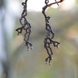 Puede incluir: Un par de pendientes de plata con un delicado diseño en forma de rama. Los pendientes están hechos de metal y tienen un acabado plateado.