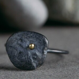 Puede incluir: Un anillo de plata oxidada negra con un peque&ntilde;o punto dorado en el centro de la cara del anillo.