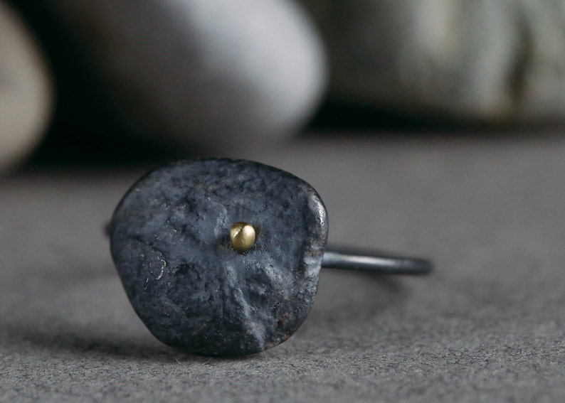 Puede incluir: Un anillo de plata oxidada negra con un peque&ntilde;o punto dorado en el centro de la cara del anillo.