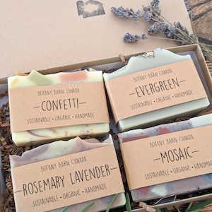 May include: Four bars of handmade soap in a gift box. The soaps are labelled "Confetti", "Evergreen", "Rosemary Lavender", and "Mosaic". Each bar is made with natural ingredients and is sustainable and organic.