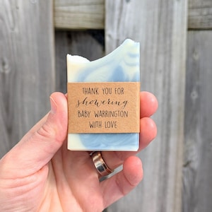 May include: A rectangular bar of soap with a marbled blue and white design, wrapped with a brown paper band. The band reads, "THANK YOU FOR showering BABY WARRINGTON WITH LOVE."
